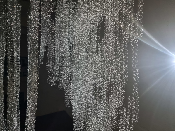 A hanging artwork made from wire being lit from the right side.
